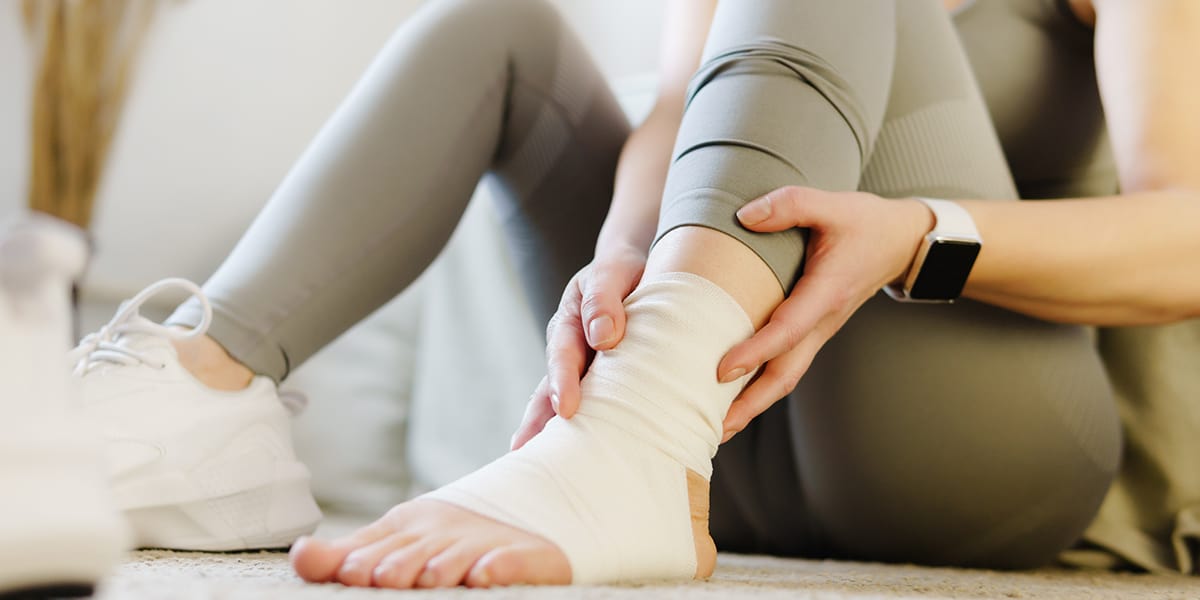 Someone using compression bandages to apply pressure to an ankle injury